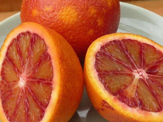 Closeup of blood oranges cut in half, showing the mottled blood orange flesh.