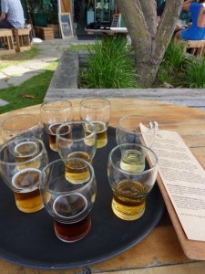 Tray of glasses of different beers, resting on a table in a garden.