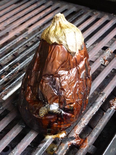 An scorched and smoky whole eggplant or aubergine sitting on a BBQ grill