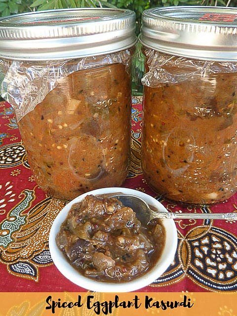 Two jars of eggplant kasundi (relish) with a small bowl of teh same relish with a spoon resting in it.