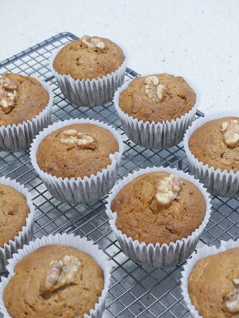 carrot cafe muffins toped with walnut pieces sit on a mesh cooling rack