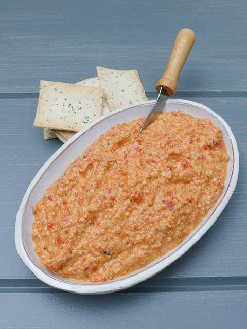 shallow dish of cashew & red pepper dip with small knife in dish and crackers beside the dish