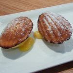 white plate with two madeleine cakes sitting on a dollop of lemon butter
