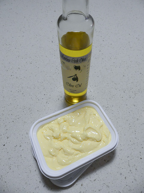 spreadable butter recipe in a plastic tub with a bottle of olive oil in background