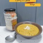 glass jar filled with lentils and spices on bench beside brown bowl of curry coconut and lentil soup