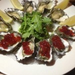 Oysters on a platter topped with salmon caviar and lemon wedges