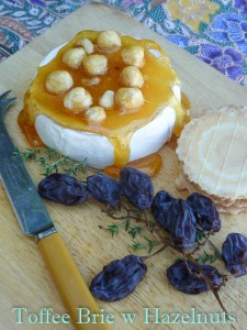 Wheel of brie cheese with hardened toffee and hazelnuts ured over the top and tumbling down the sides of the cheese