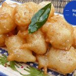 A platter of golden honey puffs drizzled with syrup and topped with icing sugar and cinnamon