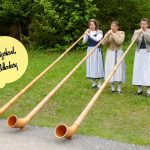 Three women in traditional folk dress play large musical horns in Ballenberg, Switzerland