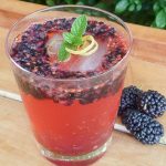 glass of mulberry cocktail with sprig of mint and curls of lemon zest